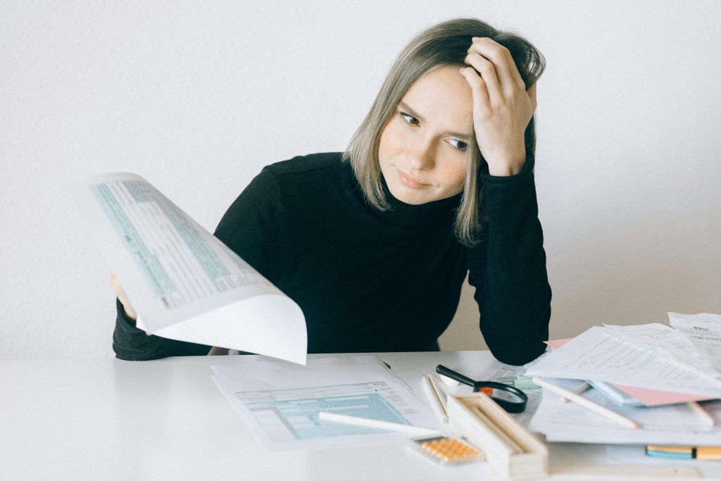 A woman showing stress while reviewing multiple paperwork and financial documents at a desk.