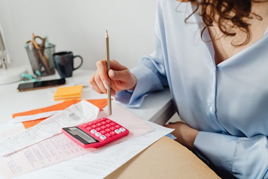 Home A woman is calculating expenses using a calculator and papers at her desk.